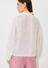 A woman wearing a white linen blouse with ruffled collar and cutwork embroidery detailing.