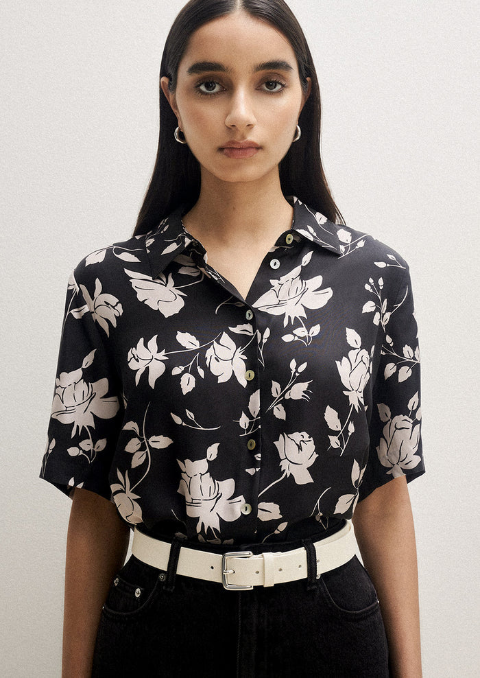 A person wearing a short sleeve collared shirt in black with white floral pattern.
