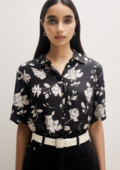 A person wearing a short sleeve collared shirt in black with white floral pattern.