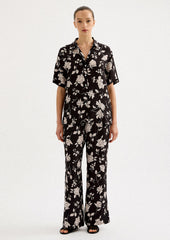 A person wearing a short sleeve collared shirt in black with white floral pattern.