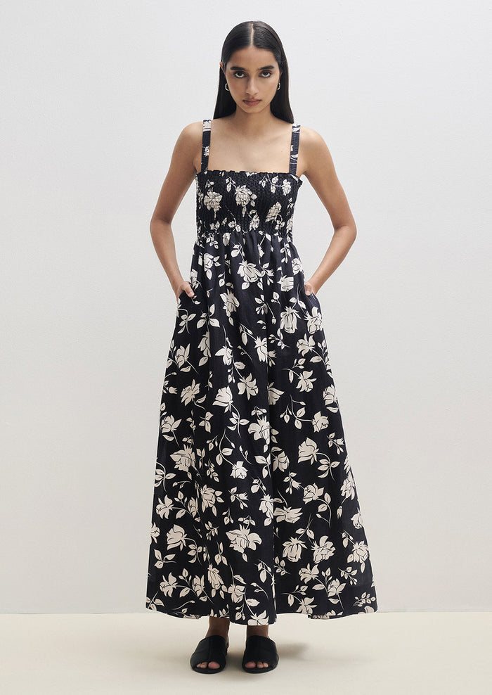 A woman wearing a black and white floral print maxi dress with smocked bodice.