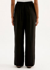 A person wearing a pair of black sateen pants with split leg hem.