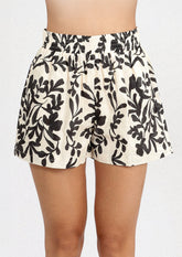 A person wearing a white pair of shorts with black leafy floral print.