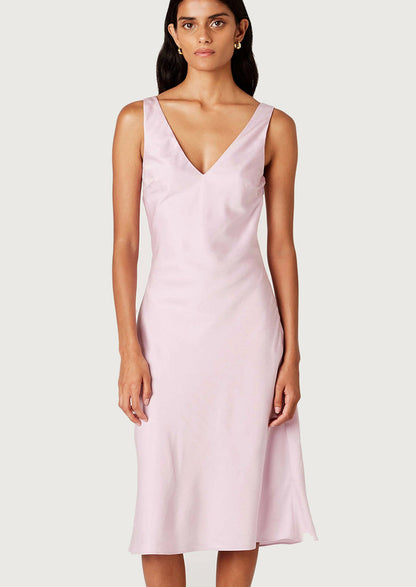 A woman wearing a satin v-neck sleeveless dress in ice pink.