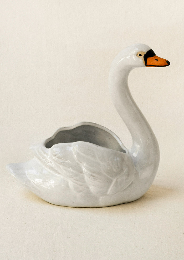 A ceramic planter in the shape of a cygnet sitting atop a table against a beige backdrop.