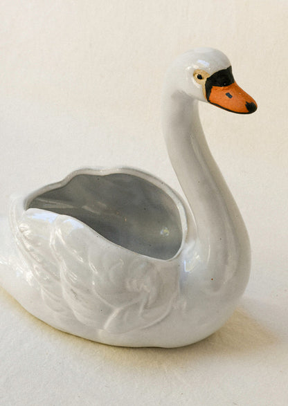 Top view of a ceramic planter in the shape of a cygnet sitting atop a table.