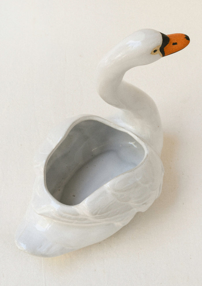 Top view of a ceramic planter in the shape of a cygnet sitting atop a table.
