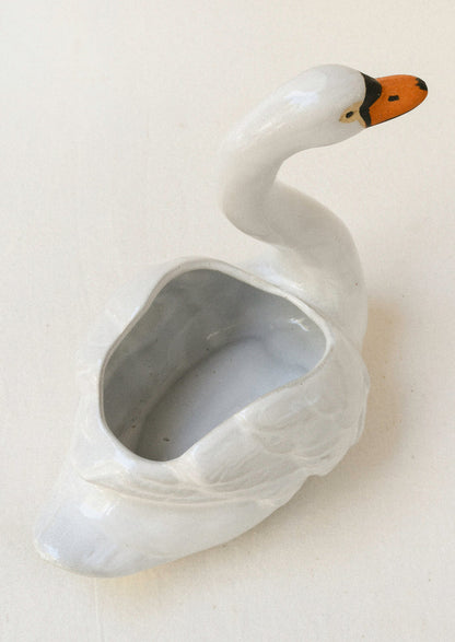 Top view of a ceramic planter in the shape of a cygnet sitting atop a table.