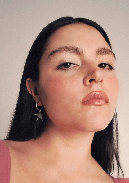 A person wearing a pair of gold star earrings on hoop.
