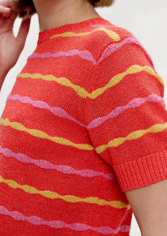 A woman wearing a red short sleeve knit top with yellow and pink wavy stripes.