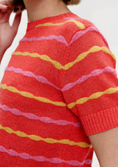 A woman wearing a red short sleeve knit top with yellow and pink wavy stripes.