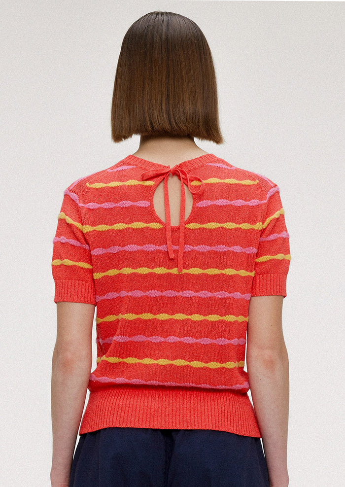 A woman wearing a red short sleeve knit top with yellow and pink wavy stripes.