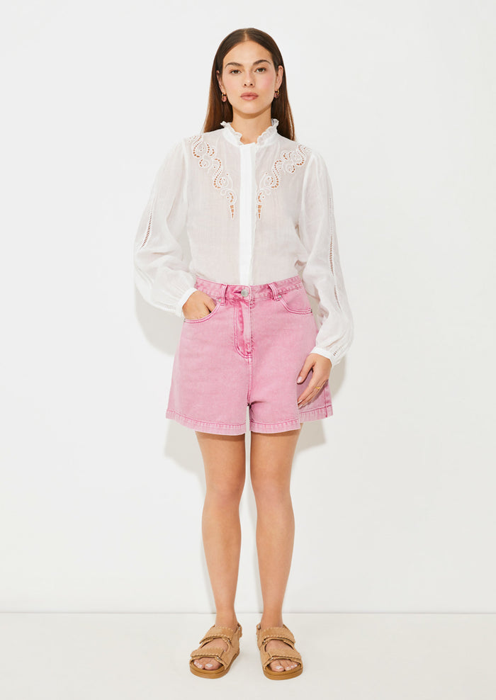 A woman wearing a white linen blouse with ruffled collar and cutwork embroidery detailing.