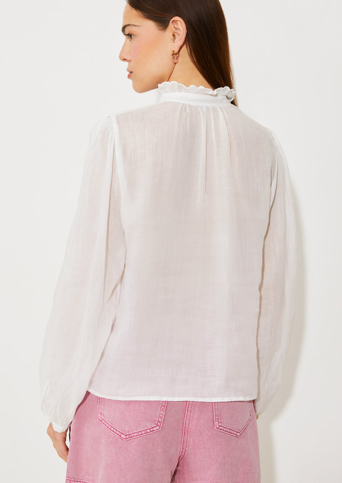 A woman wearing a white linen blouse with ruffled collar and cutwork embroidery detailing.