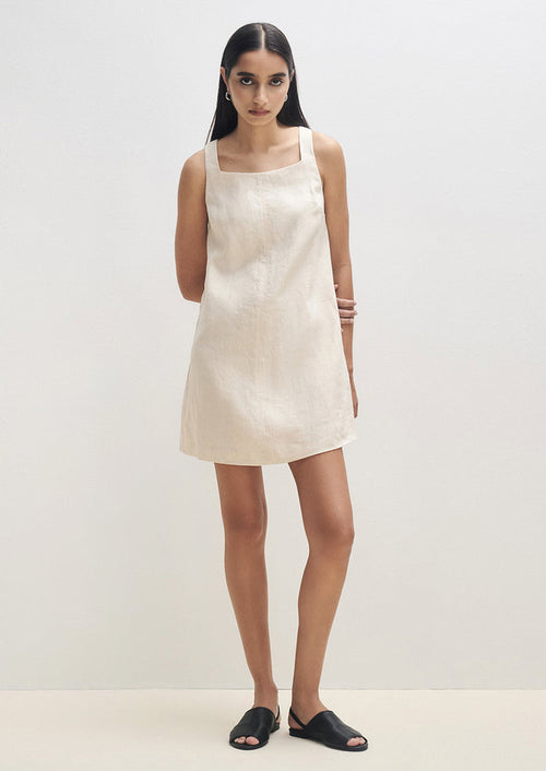 A woman wearing a natural colored linen mini dress with square neck.