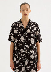 A person wearing a short sleeve collared shirt in black with white floral pattern.