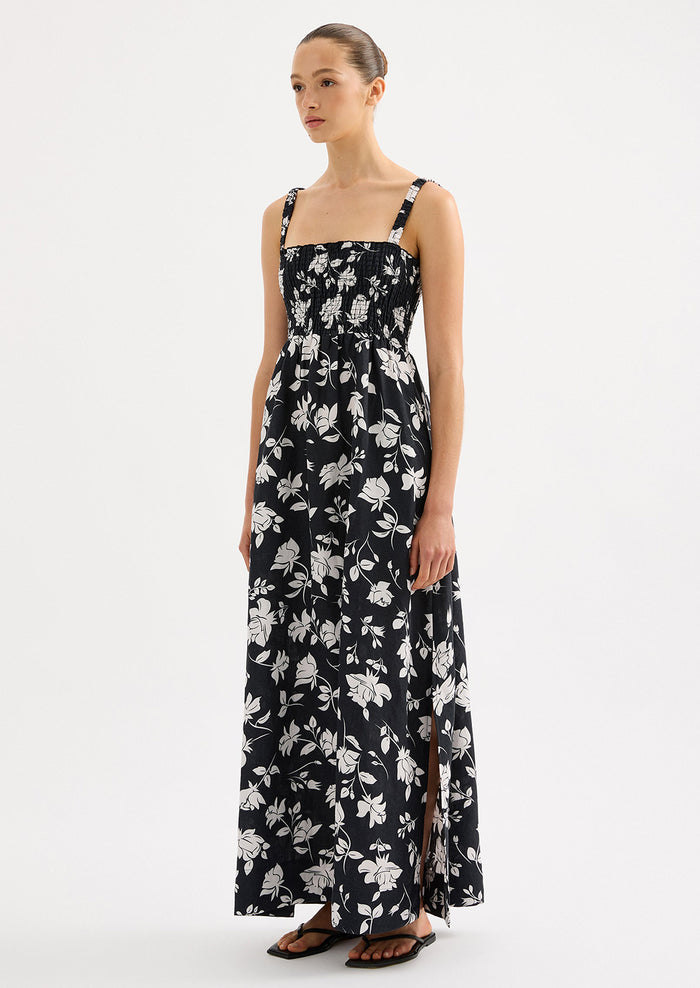 A woman wearing a black and white floral print maxi dress with smocked bodice.