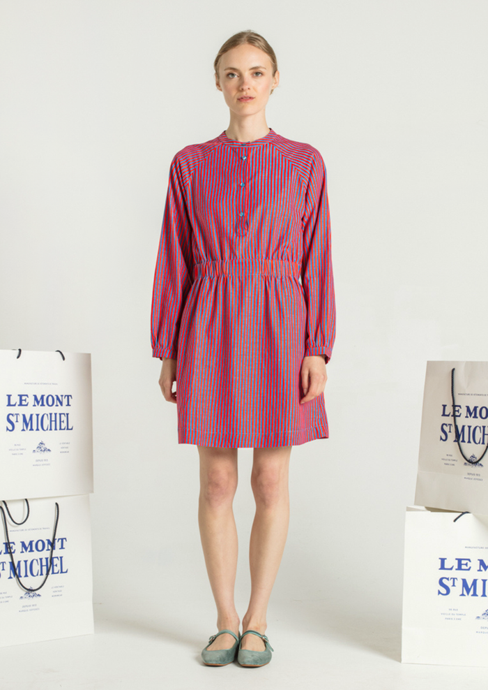 A woman wearing a long sleeved short dress in blue and red vertical stripe pattern.