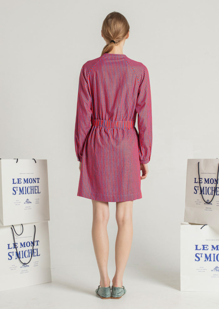 A woman wearing a long sleeved short dress in blue and red vertical stripe pattern.