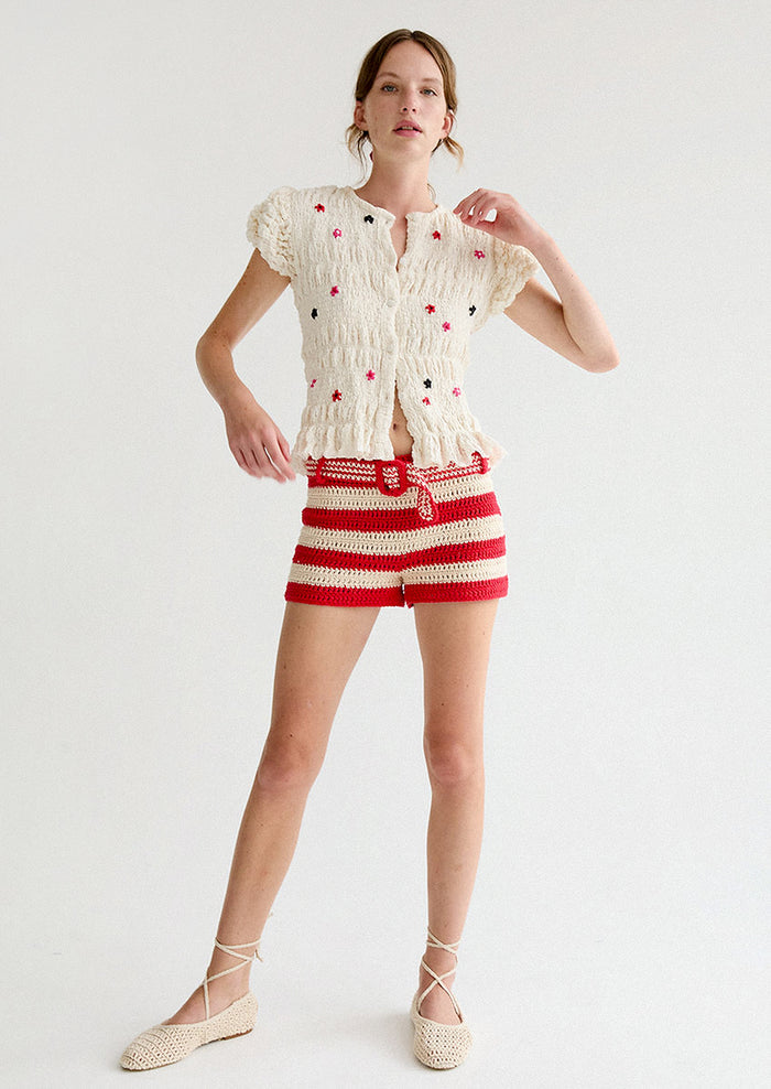 A woman wearing a smocked and ruffled cream top with red and pink embroidered flowers throughout.