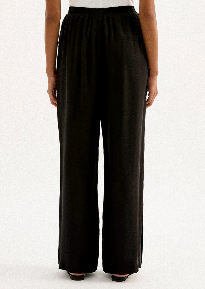 A person wearing a pair of black sateen pants with split leg hem.