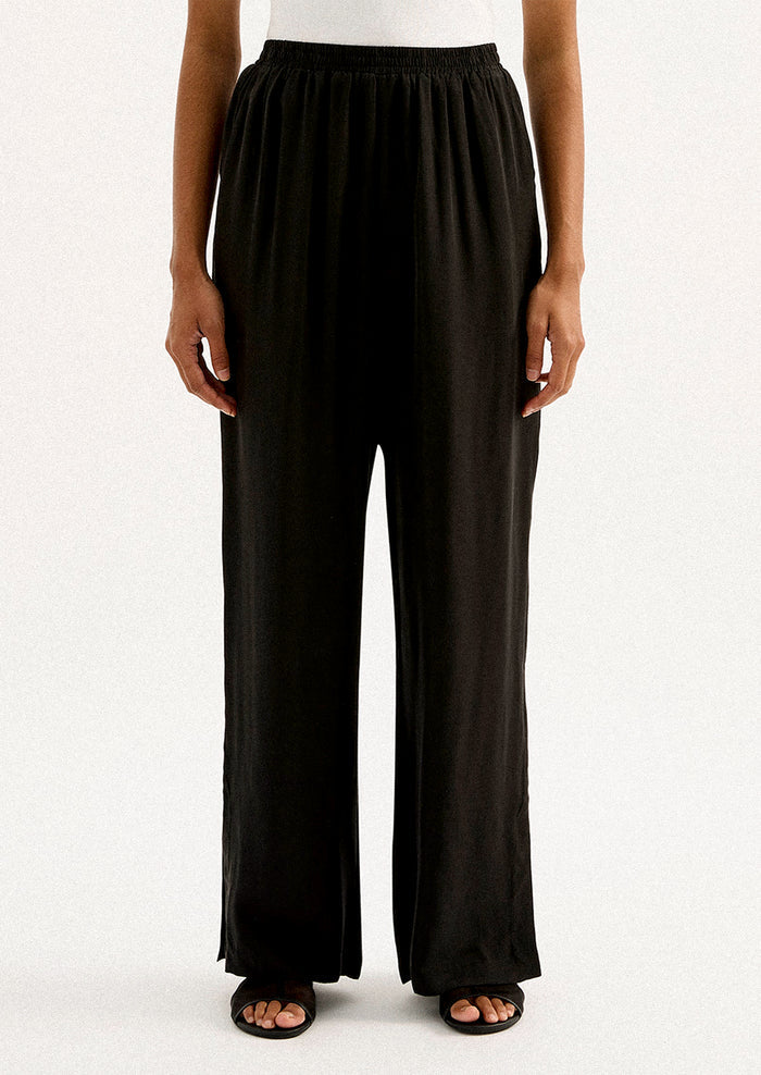 A person wearing a pair of black sateen pants with split leg hem.