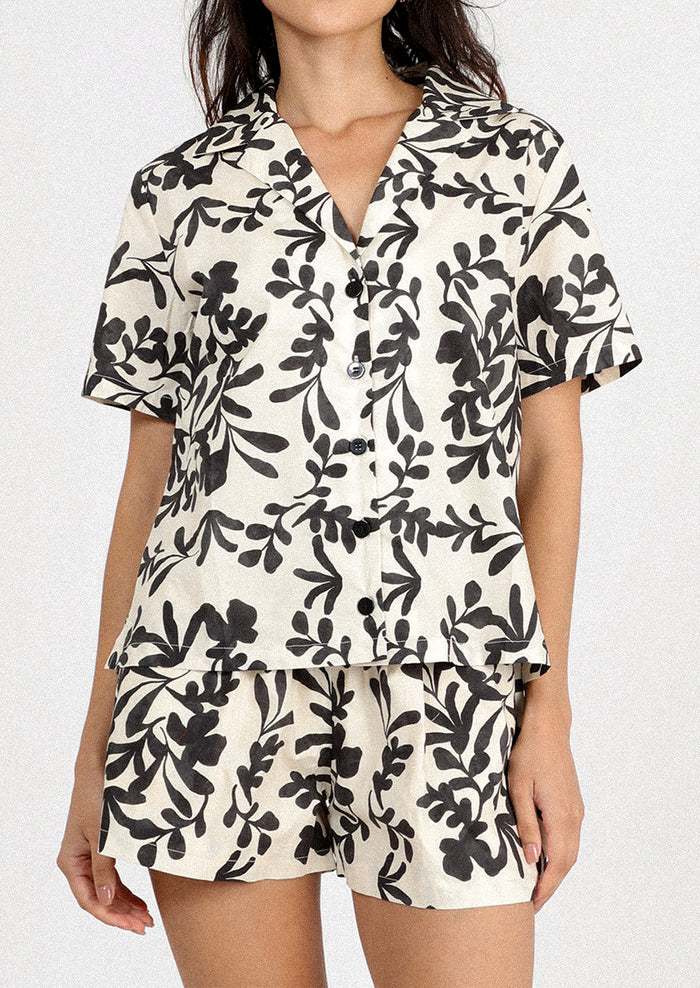 A person wearing a white pair of shorts with black leafy floral print.