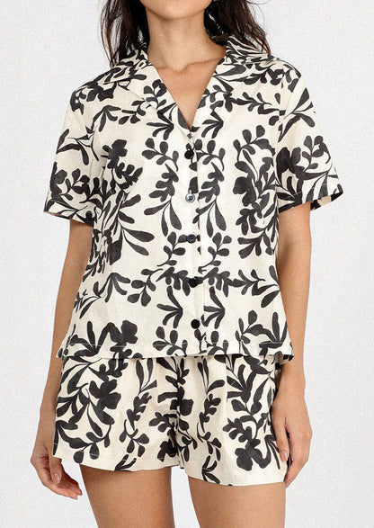 A person wearing a white pair of shorts with black leafy floral print.