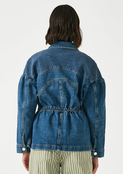 A woman wearing a denim jacket with decorative stitching and ruched shoulder detail.
